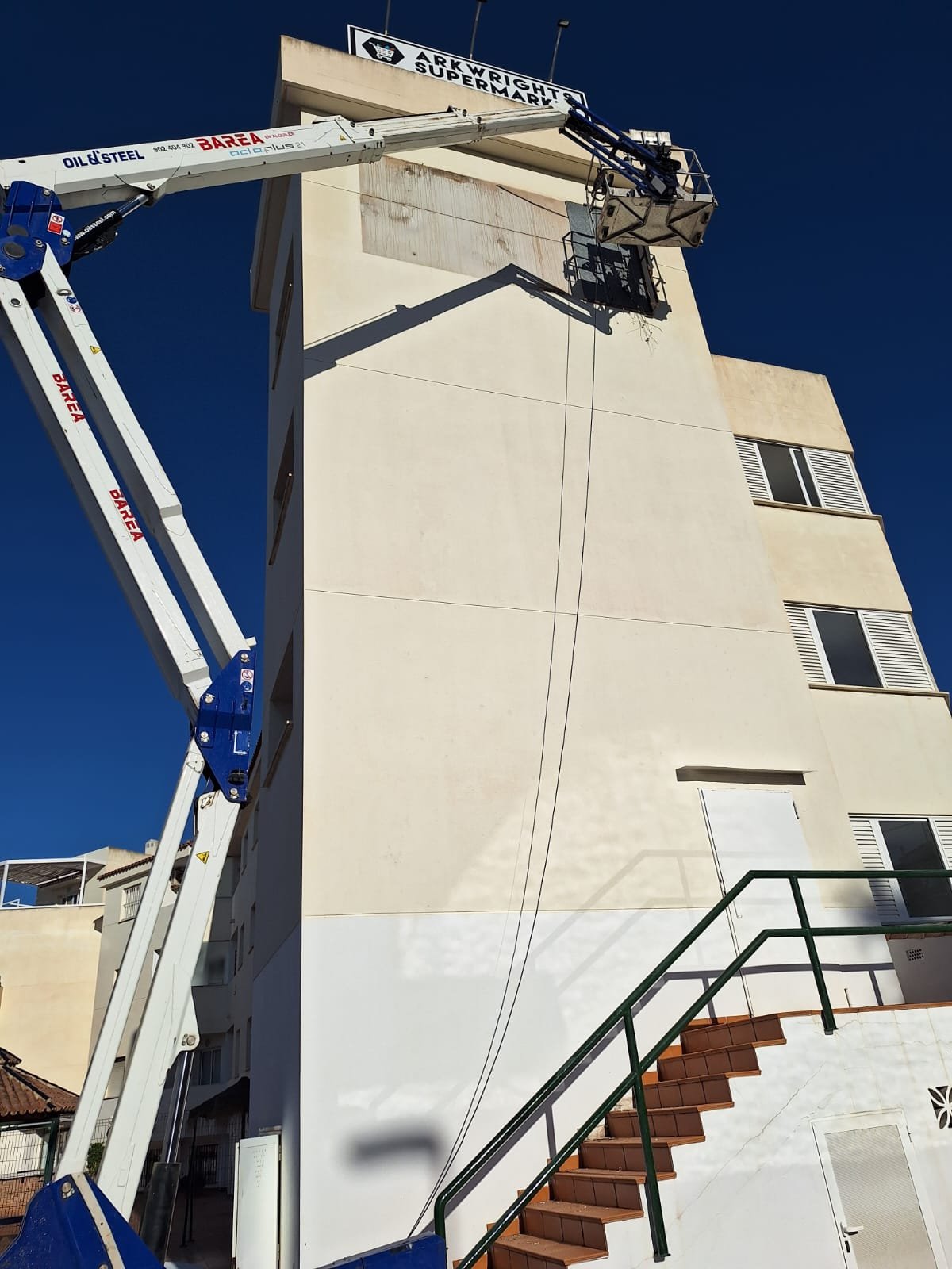 Plataforma elevadora trabajando en altura sobre fachada de supermercado